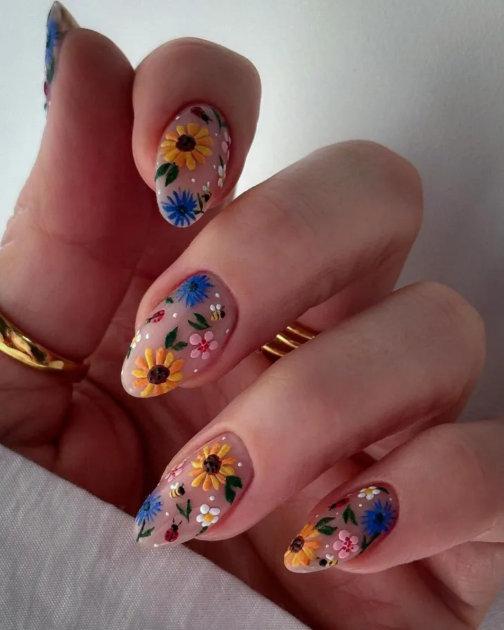 Floral nails design with French tip flower patterns - creative hand showcasing light pink base with white French tips, featuring colorful flower petals and green leaves on almond-shaped nails